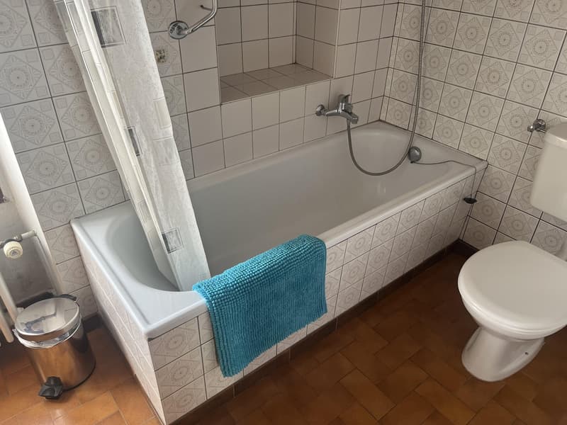 white tiled walls, brown tiled floor, bathtub, shower curtain, towel, toilet