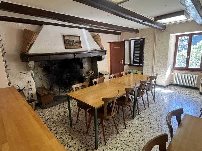 Dining room with wooden table, chairs, fireplace, open door, window, radiator, storage boxes, and broomsticks.