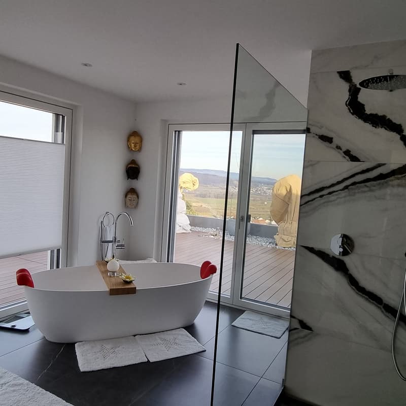 Modern bathroom with a large bathtub, glass doors, marble floor, white towels, showerhead, and window