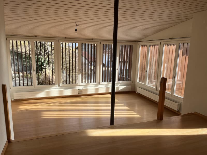 large room with wooden floor, high ceiling, glass windows, several pillars
