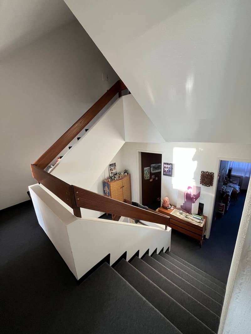 white staircase with wooden handrail, carpeted steps, wooden cabinet, picture frames, and a desk with items