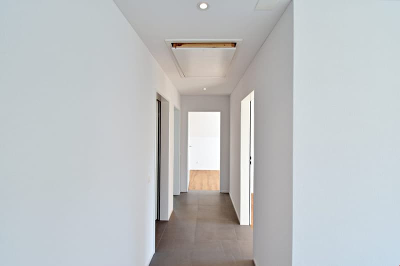 Empty hallway with white walls, wooden floor, and ceiling lights