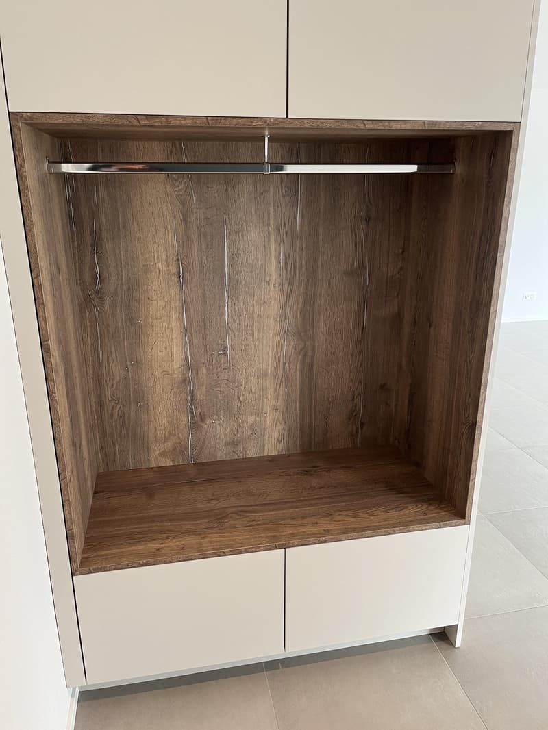 Close up of a wooden wardrobe with a metal rod, wooden shelf, and white cabinets