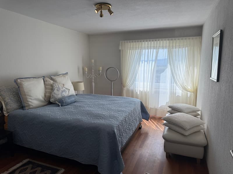 large bed with blue cover, white nightstand, mirror, lamp, window with curtains, picture frame