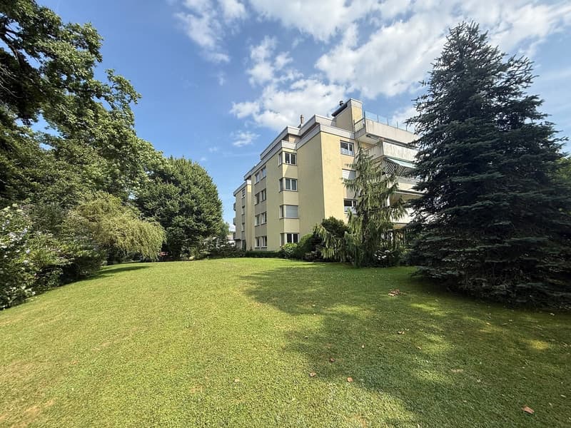 large multi-story yellow building with many windows, large green lawn in front