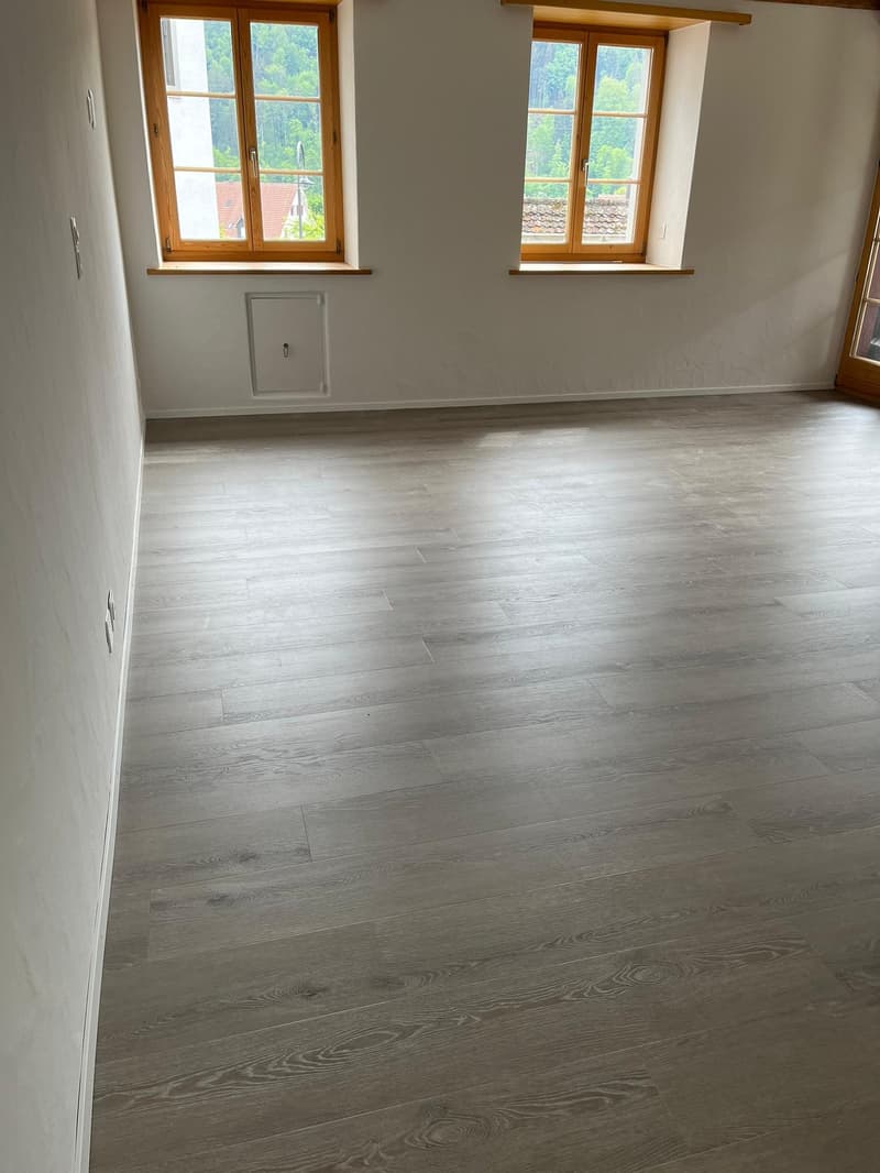 empty room with two large windows, wooden floors, power outlets
