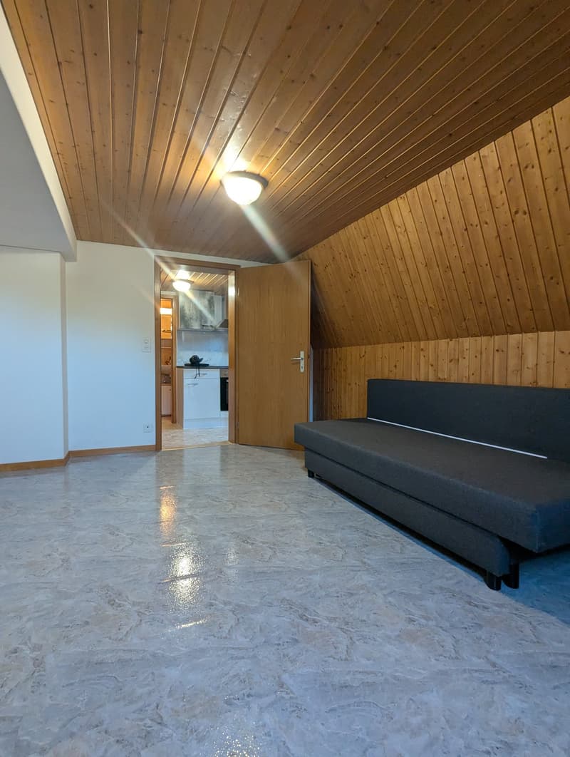 Empty room with wooden ceiling, white floor, a couch, and an open door leading to a kitchen.
