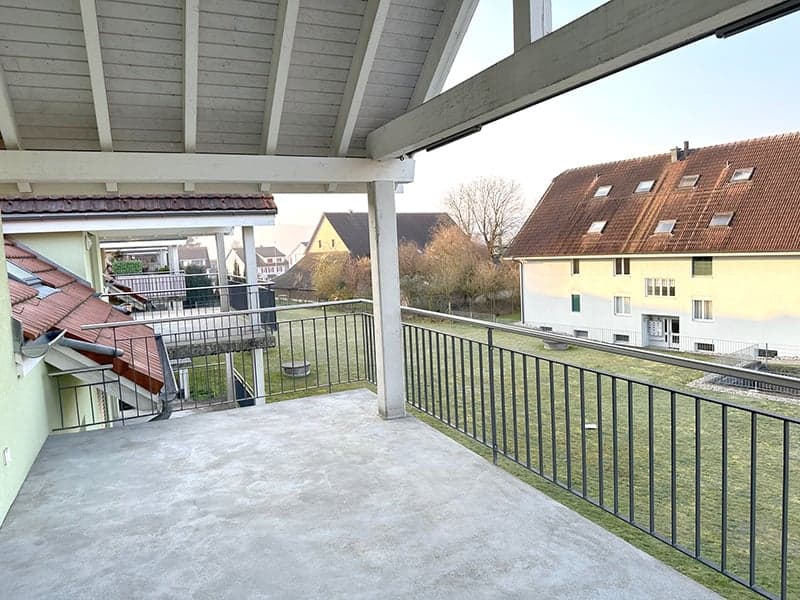covered balcony, metal railing, concrete floor, view of a grassy area and buildings