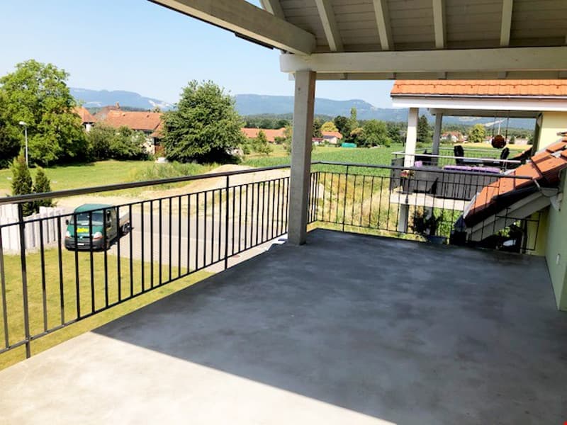 covered balcony, black railings, concrete floor, view of a field and mountains