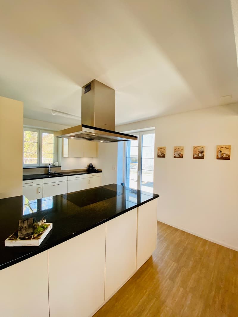 modern kitchen with black granite countertop, white cabinets, stainless steel range hood, induction cooktop, sink, faucet, and framed pictures on the wall