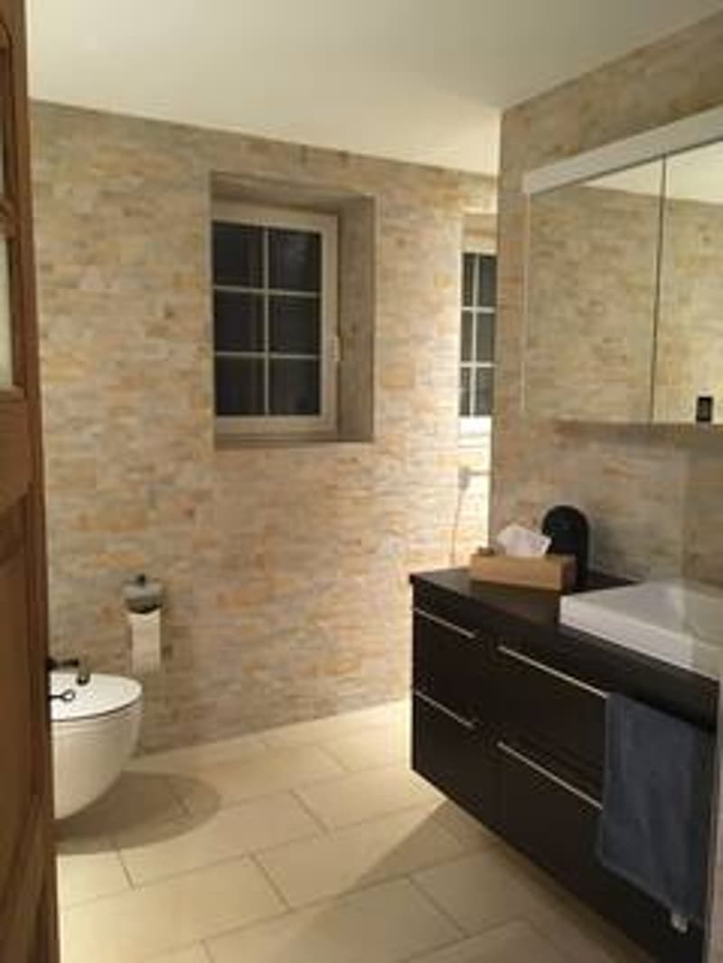 Bathroom with white toilet, sink, mirror, and tiled walls
