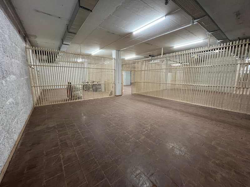 Empty large storage space with a brick floor, high ceilings with exposed beams and lights