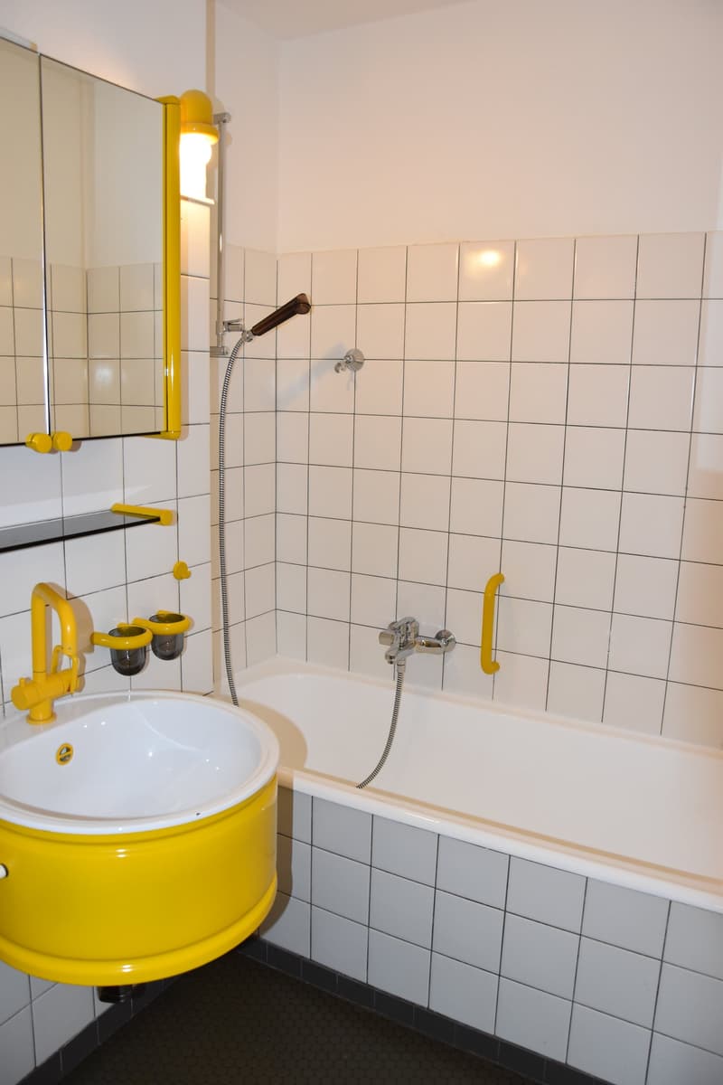 Bathroom with white tiles, white bathtub, yellow sink, yellow fixtures, and mounted mirror