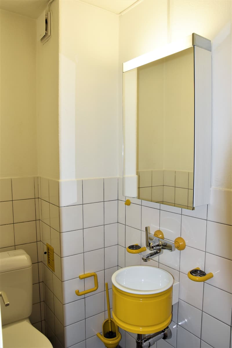 small white bathroom with yellow sink, white toilet, tiled walls, and yellow fixtures