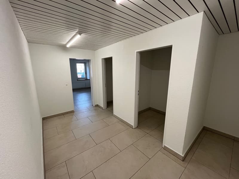 Empty hallway with tiled floor, white walls, two doors, ceiling lights