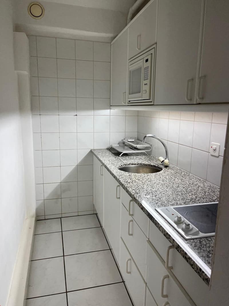 white tiled wall, white tiled floor, granite countertop, stainless steel sink, microwave, dishwasher, electric stove, cabinets, power outlet