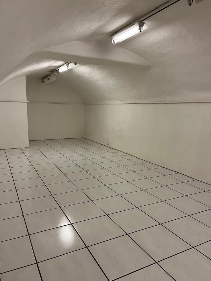 An empty room with white tiled floor, white walls, and mounted ceiling lights.