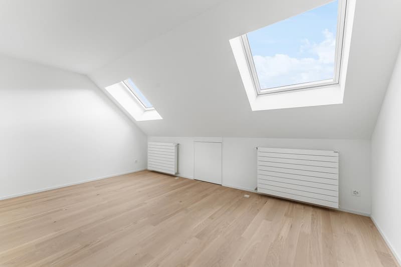 Empty room with wooden floor, two white radiators, and two skylights.