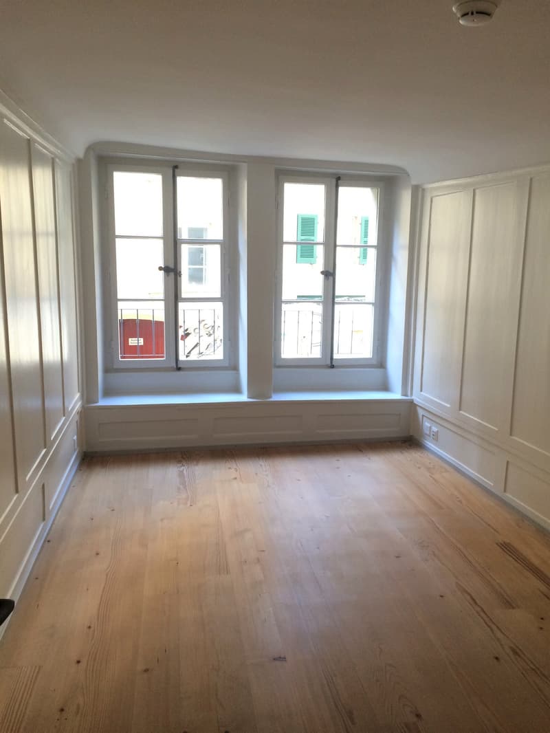 room with white walls, hardwood floors, white doors, large windows with built-in window seats