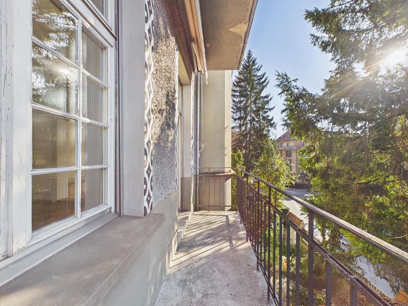 Balcony with railings, large windows, concrete floor, trees in the background