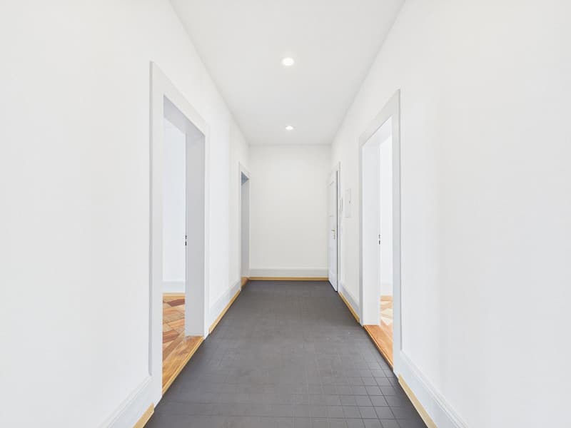 Empty hallway with white walls, gray floor, wooden trims, and doors on both sides.