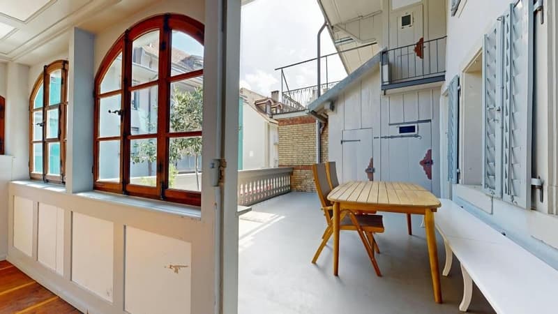 wooden floor, large arched window, wooden table and chairs, white walls, balcony