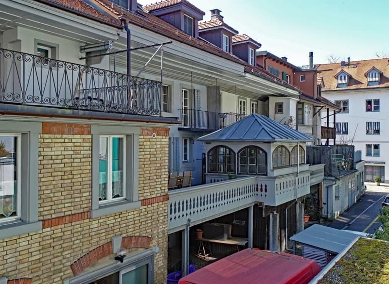 multi-story building, brick facade, multiple balconies, metal railings, windows with white frames, a car parked on the street