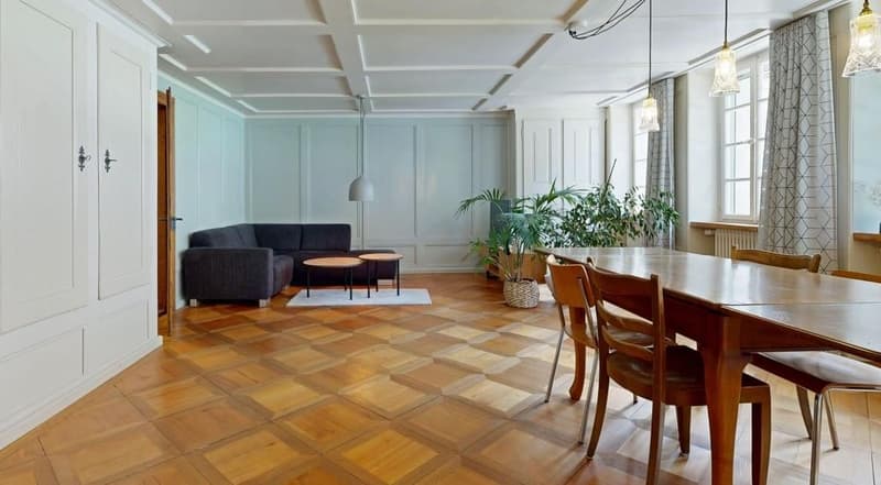 wooden floor, white walls, gray couch, coffee table, dining table, chairs, plants, lamps