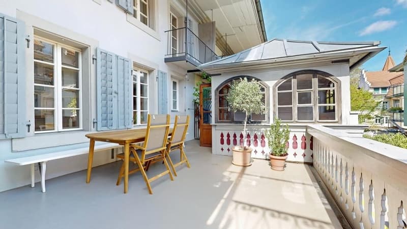 white house, blue shutters, wooden table and chairs, white bench, potted plants, balcony