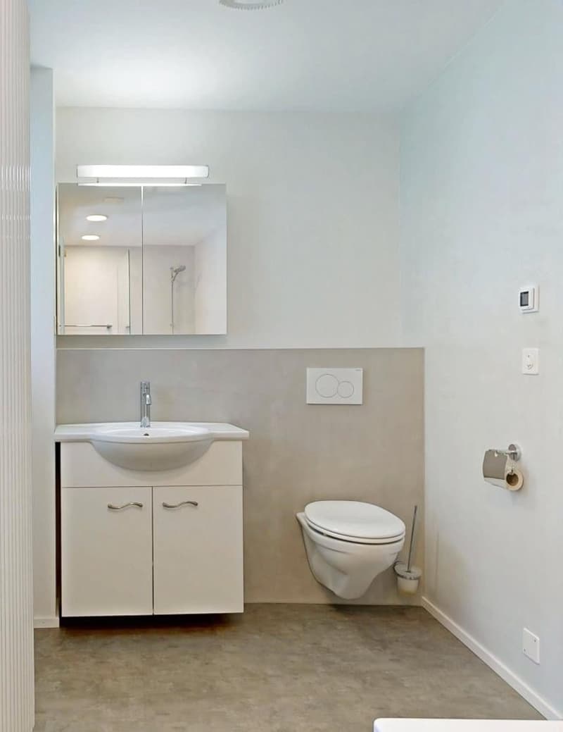 small bathroom with white sink, white toilet, white cabinet, mirror with light, tiled floor