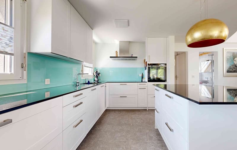 modern kitchen with white cabinets, blue-green backsplash, white counters, black tiles, brass pendant light, modern appliances, tiled flooring