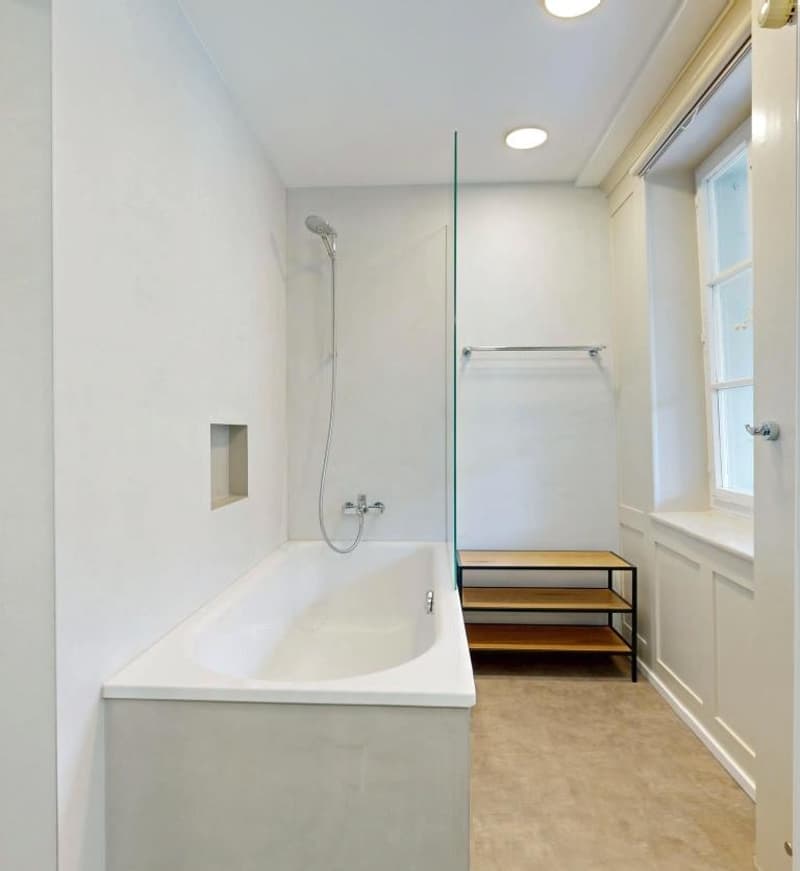 white bathtub, shower head, glass door, wooden shelf, white walls, window