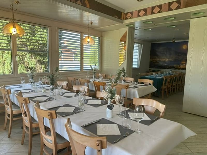 A dining room with tables and chairs set for a meal, glass windows, wooden ceiling, decorative wall art, wooden floor.