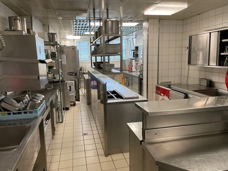 modern commercial kitchen with stainless steel countertops, multiple sinks, ovens, fridges, shelves, and equipment
