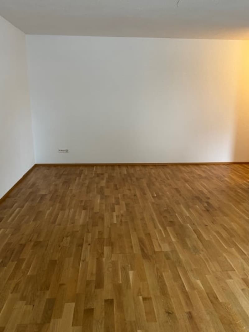 Wooden floor, white walls, outlet on wall, bright light illuminating room
