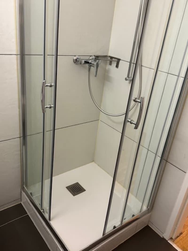 The image shows a modern bathroom with a glass shower enclosure, a shower head, and a tiled floor.