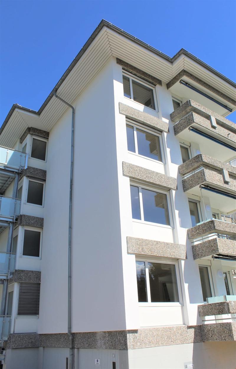 Multi-story residential building, white exterior, balconies on upper floors, large windows, modern architecture, grey stone accents, flat roof with ridge tiles