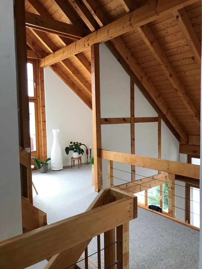 Carpenter style interior, white and brown walls, white carpet, wooden ceiling and railings, wooden columns, tall window