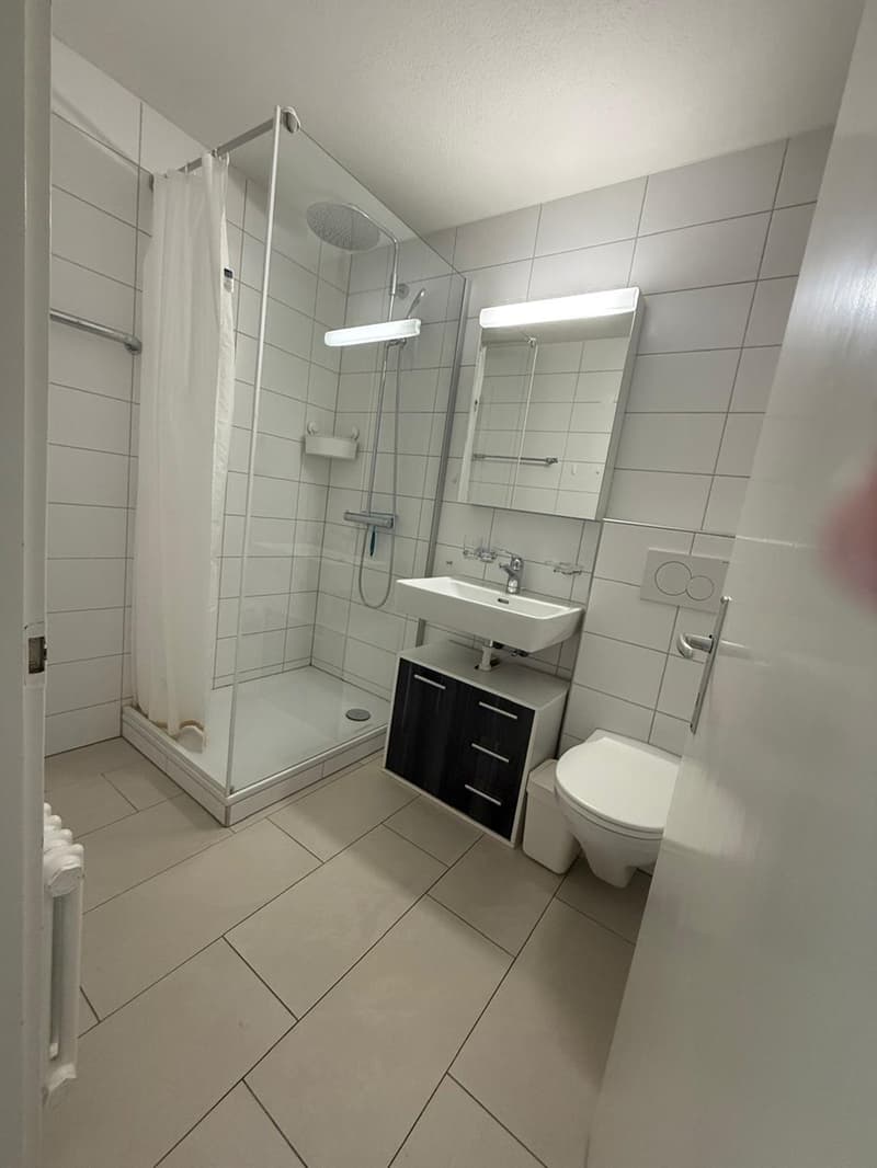 white tiled floor, white tiles, white shower cubicle, white vanity with sink, toilet, white shower curtain, illuminated mirror, light over mirror