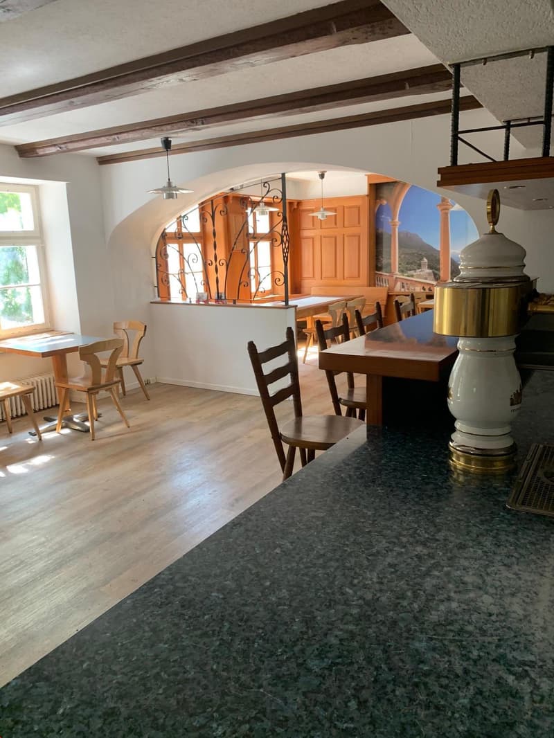 Rustic dining room with wooden beams on the ceiling, wooden tables and chairs, a fireplace, and a decorative vase on the counter.