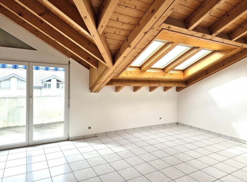 Spacious room with wooden beamed ceiling, large windows, and tiled flooring.