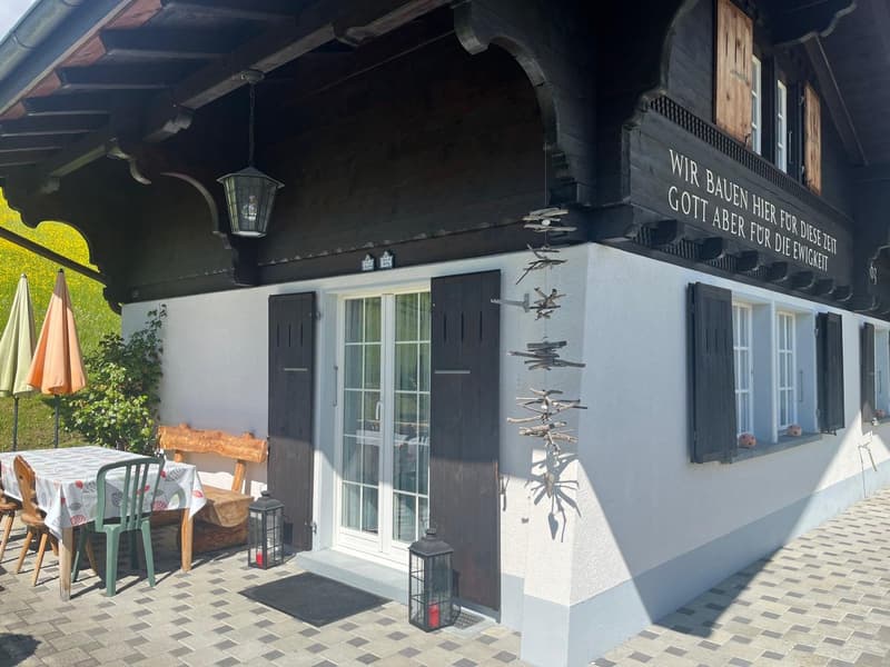 Black and white exterior, black roof, wooden front door, balcony with table and chairs, awning, plants