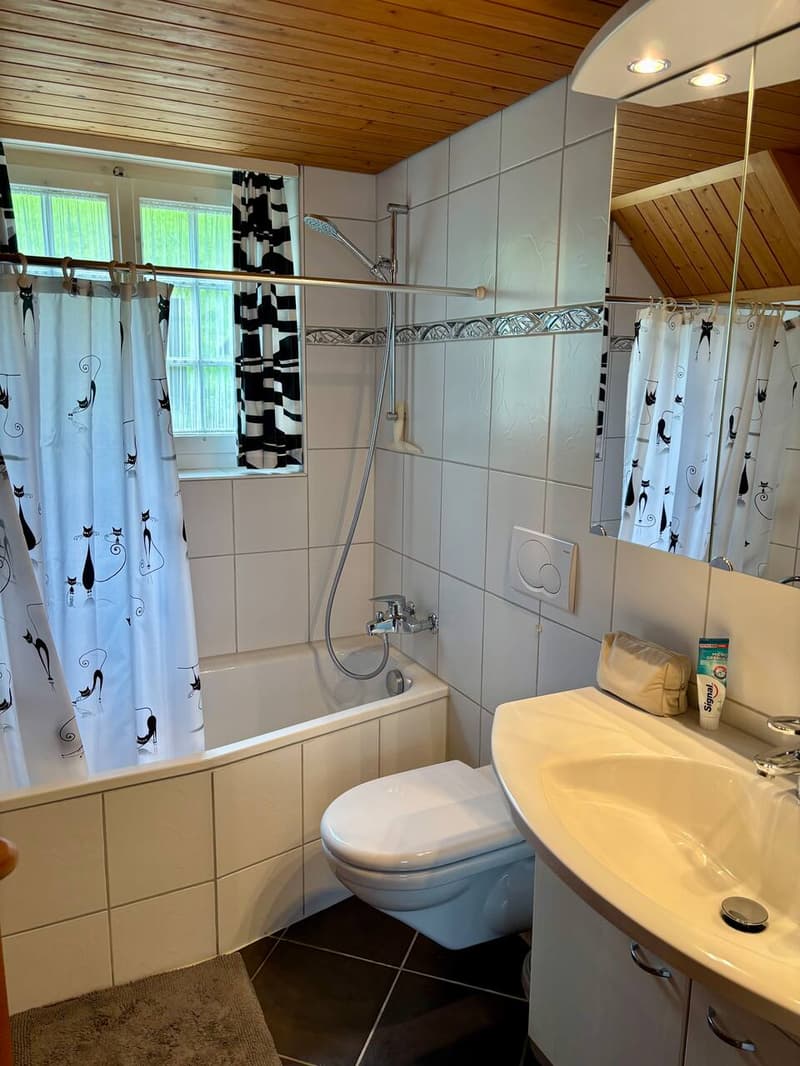 A white tiled bathroom with a bathtub, toilet, sink, and mirror.