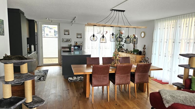 Dining room with wooden table, brown chairs, kitchen island, wooden floor, white curtains, wooden cabinet, microwave, cat tree, rug