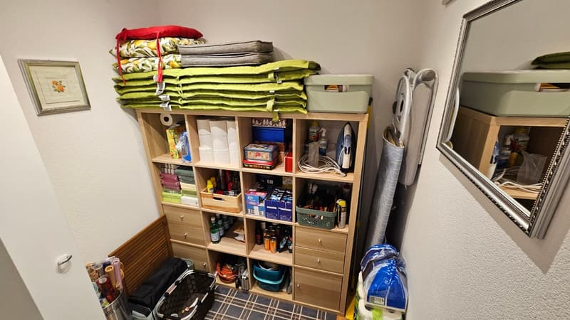 Storage room with shelves, storage boxes, cleaning products, and a mirror