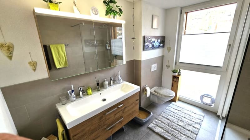 modern bathroom with double sink, shower, toilet, and window