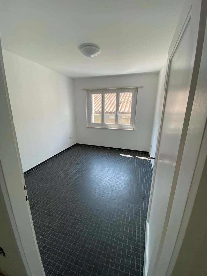 Empty room with white walls, black tiled floor, large window with view outside, ceiling light