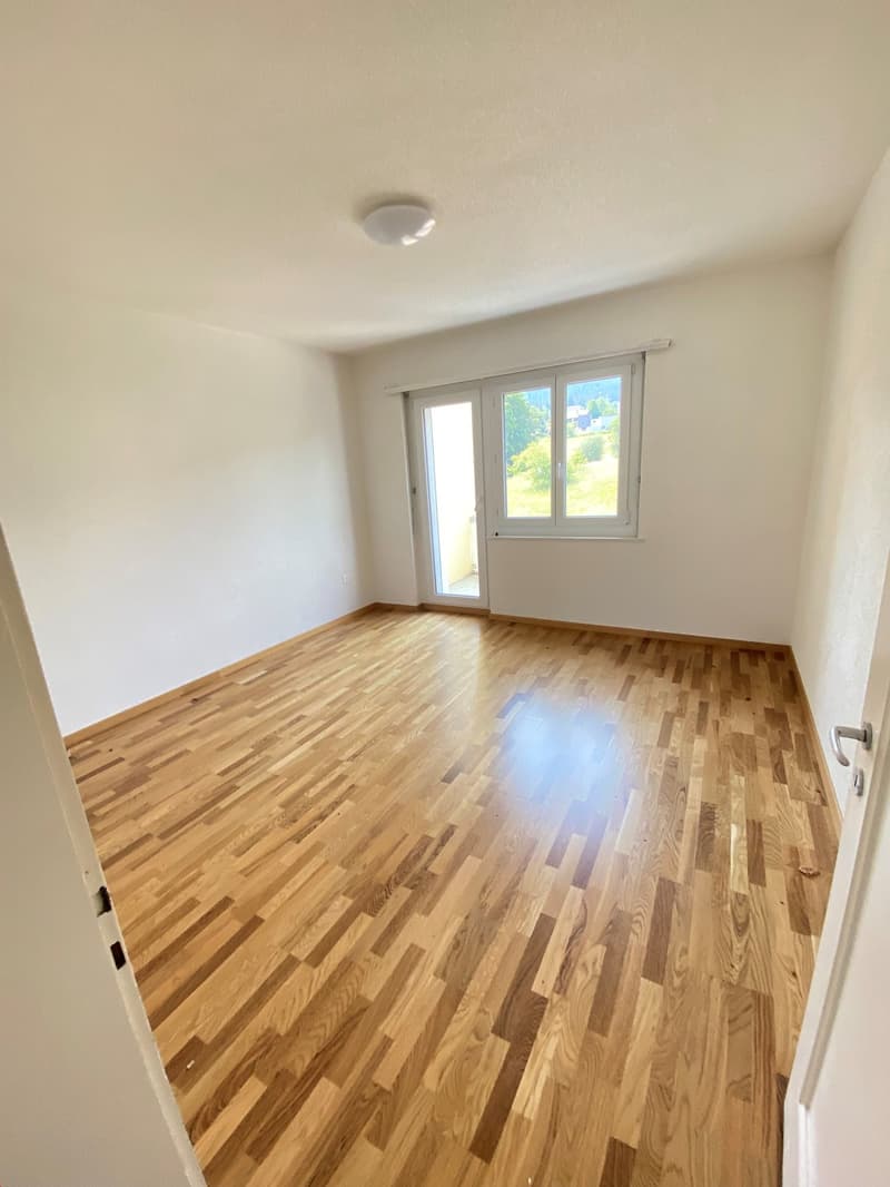 large empty room with wooden floor, large windows, sliding glass door to balcony