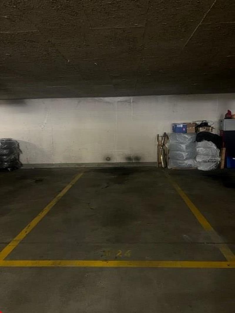 Parking space for one vehicle, grey concrete floor, yellow parking line, storage on side, no vehicles present