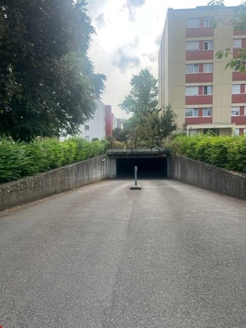 an empty parking lot beneath an overpass with gray concrete barriers and surrounded by greenery